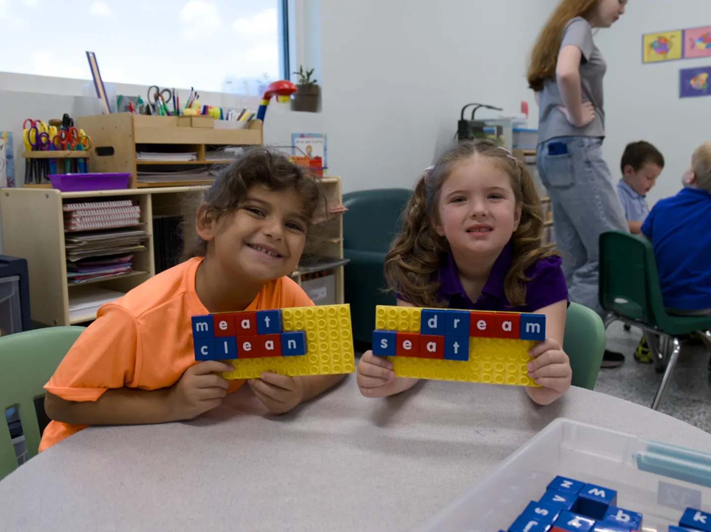 Two first graders hold up letter-tile boards spelling the words meat, clean, dream, and seat.