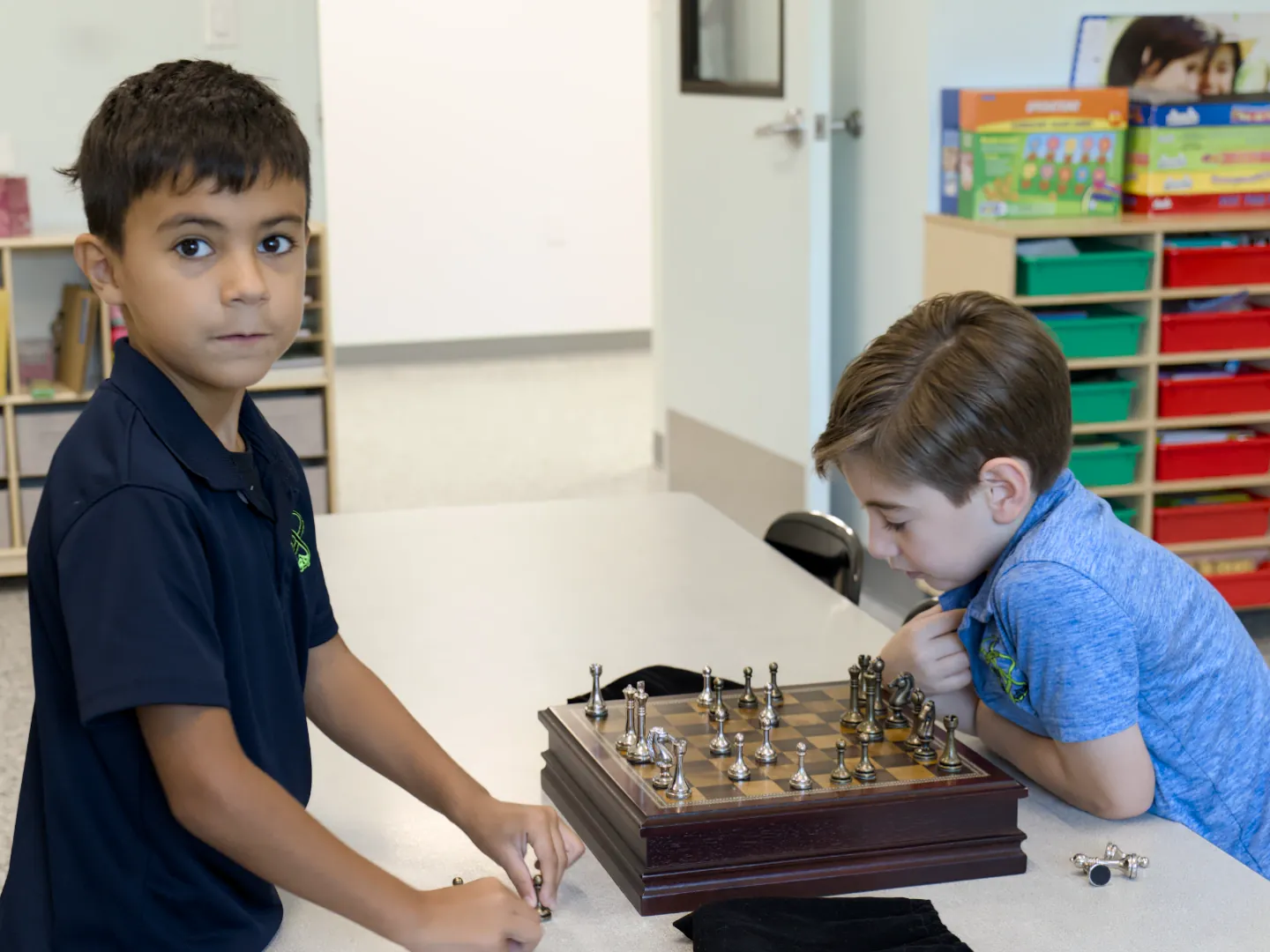 Two second graders play chess at a classroom table.
